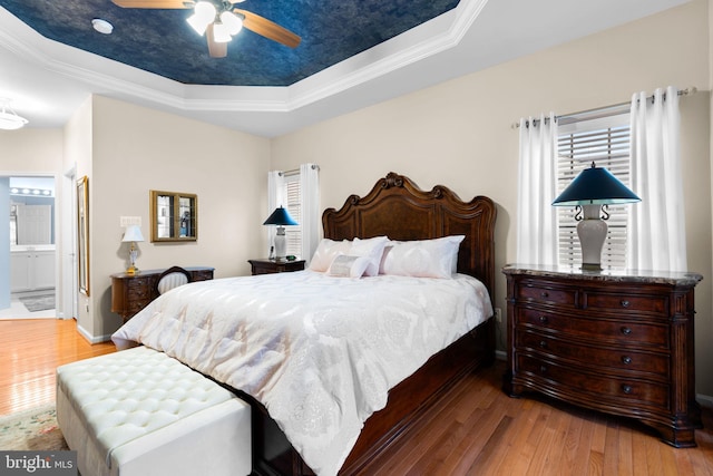 bedroom with a raised ceiling, ornamental molding, a ceiling fan, hardwood / wood-style flooring, and ensuite bath