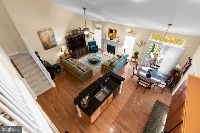 living room with light wood-style floors, ceiling fan with notable chandelier, a glass covered fireplace, and lofted ceiling