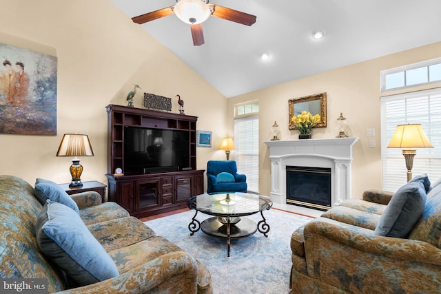 living room featuring a wealth of natural light, a glass covered fireplace, vaulted ceiling, and a ceiling fan
