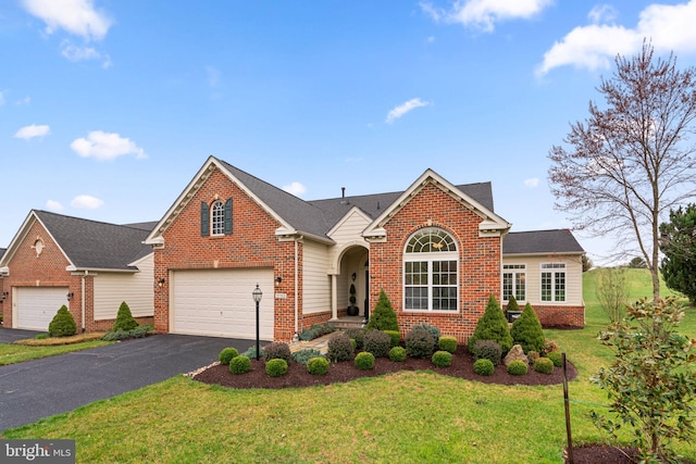 traditional home with an attached garage, aphalt driveway, a front lawn, and brick siding