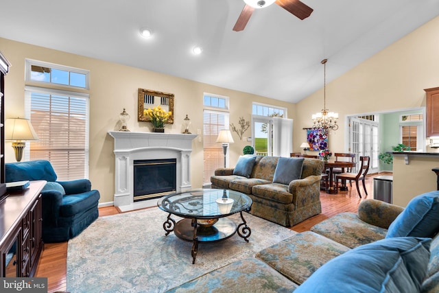 living area with ceiling fan with notable chandelier, light wood-style flooring, a glass covered fireplace, vaulted ceiling, and recessed lighting