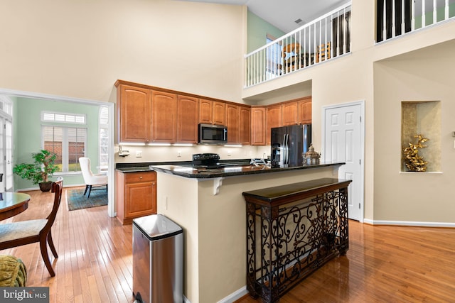 kitchen featuring light wood-style floors, baseboards, black appliances, and a breakfast bar area