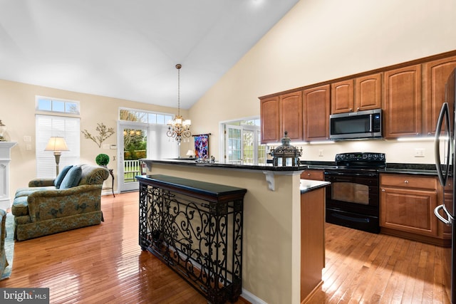 kitchen featuring a kitchen bar, light wood-type flooring, stainless steel microwave, black electric range, and dark countertops