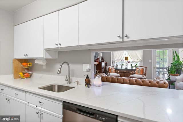 kitchen featuring white cabinetry, stainless steel dishwasher, light stone counters, and a sink