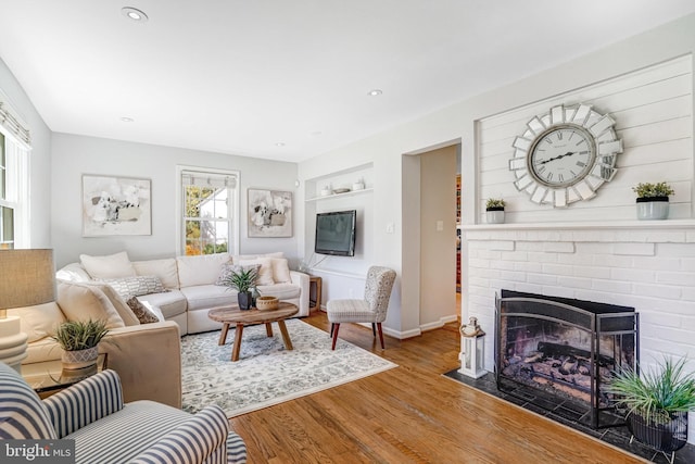 living area with baseboards, built in features, recessed lighting, a brick fireplace, and wood finished floors
