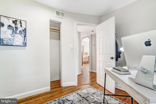 home office featuring arched walkways, visible vents, baseboards, and wood finished floors