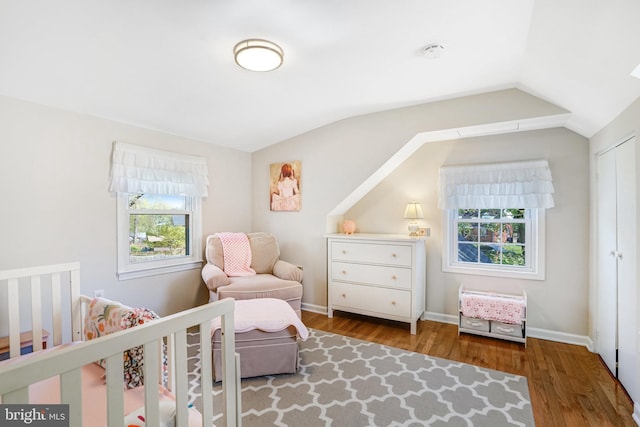 bedroom featuring wood finished floors, vaulted ceiling, and a nursery area