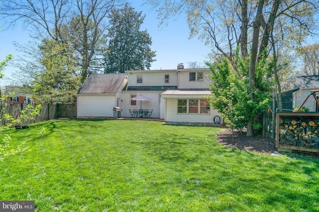rear view of property featuring a shingled roof, a chimney, fence, and a lawn