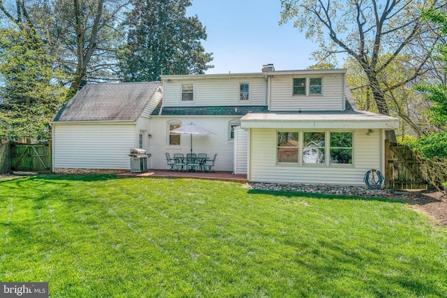 back of property with fence, a chimney, a gate, and a lawn