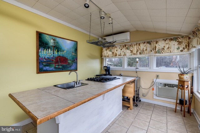 kitchen featuring tile counters, black gas stovetop, lofted ceiling, a sink, and exhaust hood