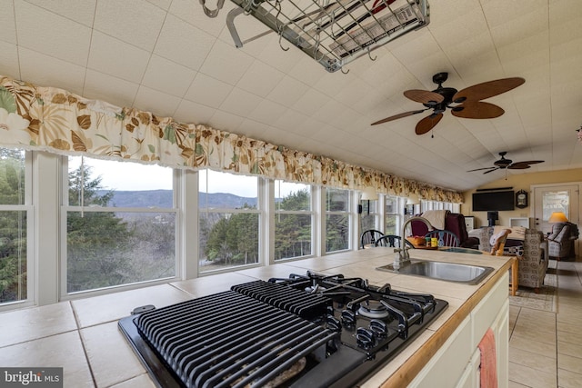 kitchen featuring light tile patterned flooring, black gas stovetop, ceiling fan, a sink, and vaulted ceiling
