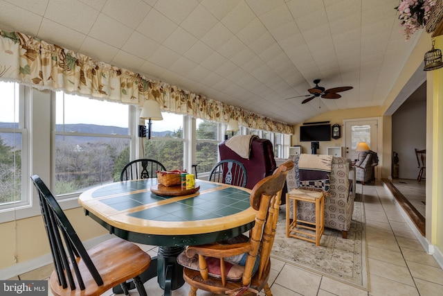 dining space featuring lofted ceiling, light tile patterned floors, baseboards, ceiling fan, and a mountain view