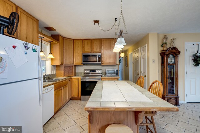 kitchen featuring light tile patterned floors, backsplash, a sink, tile countertops, and appliances with stainless steel finishes