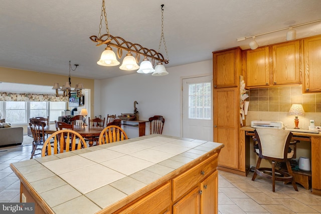 kitchen featuring tile counters, an inviting chandelier, light tile patterned floors, a textured ceiling, and backsplash
