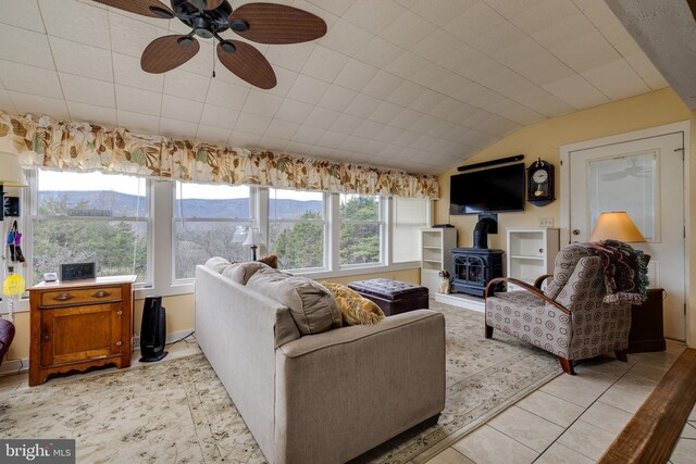 living area with a ceiling fan, light tile patterned floors, vaulted ceiling, and a wood stove