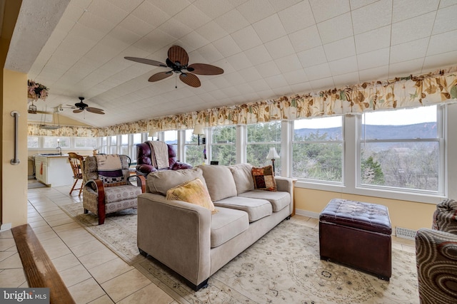 living area with a ceiling fan, visible vents, vaulted ceiling, and light tile patterned floors