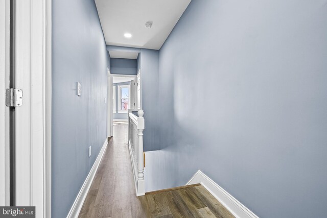 hallway with an upstairs landing, baseboards, and wood finished floors