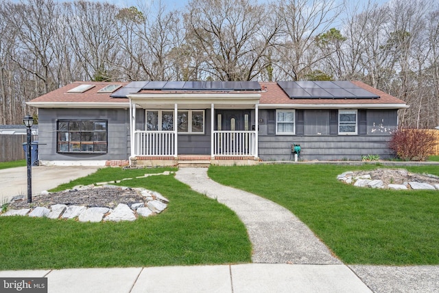 ranch-style house featuring a front yard, a porch, roof with shingles, and roof mounted solar panels