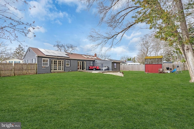 rear view of house featuring a fenced backyard, french doors, and a storage shed