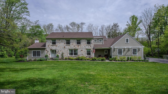 colonial-style house featuring stone siding, a front yard, and a chimney