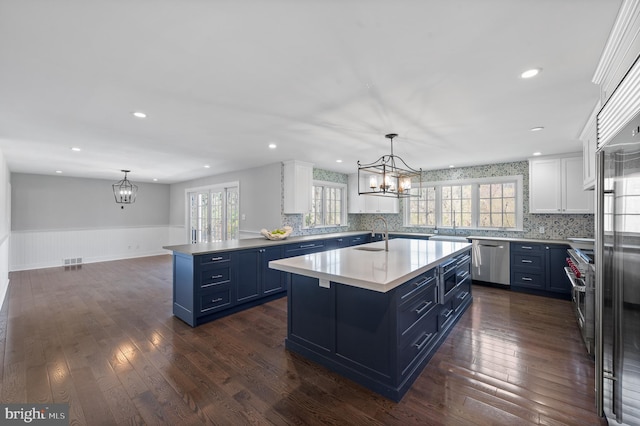 kitchen featuring wainscoting, blue cabinetry, an inviting chandelier, and stainless steel appliances
