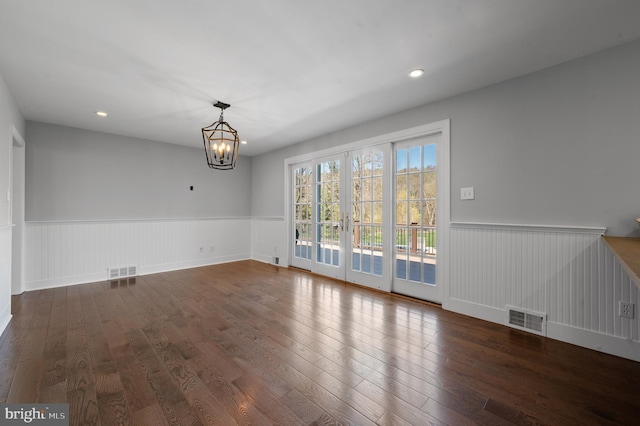 unfurnished dining area with an inviting chandelier, a wainscoted wall, wood finished floors, and visible vents