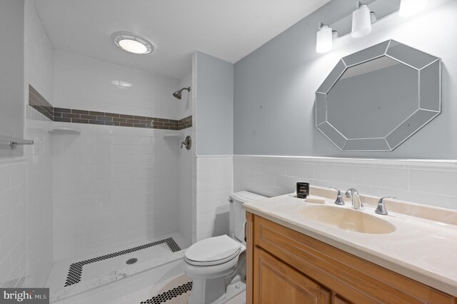 bathroom featuring vanity, toilet, tiled shower, and a wainscoted wall