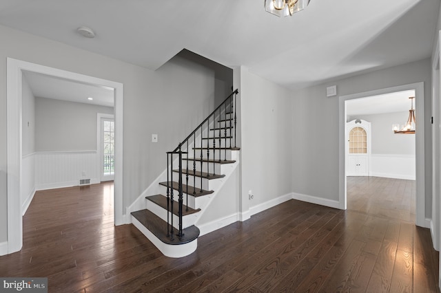 stairway featuring baseboards, visible vents, hardwood / wood-style flooring, and an inviting chandelier