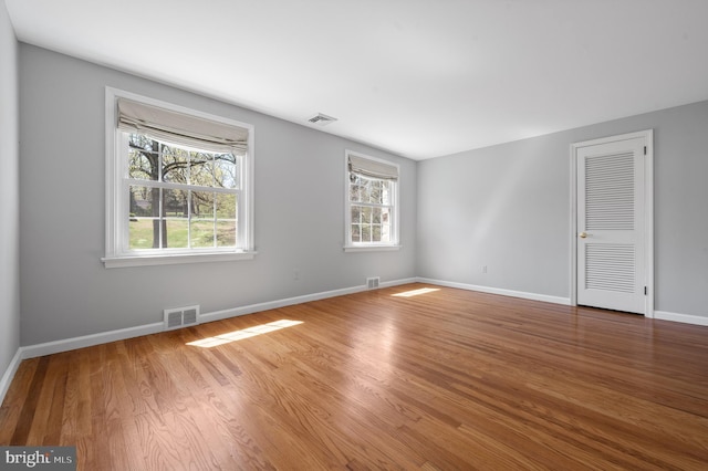unfurnished room featuring plenty of natural light, visible vents, and wood finished floors