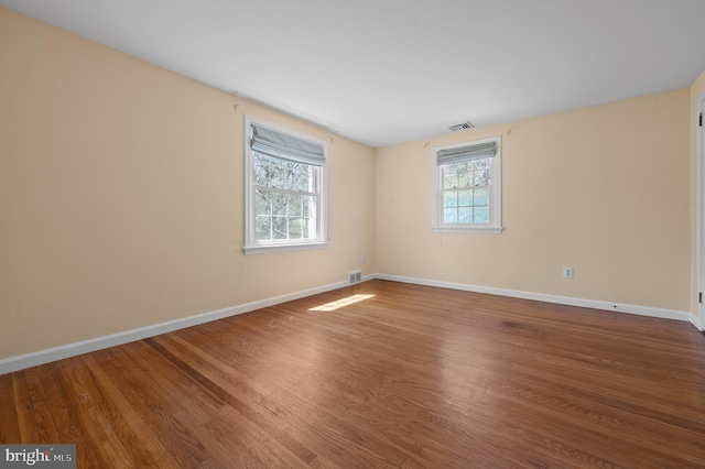 empty room with wood finished floors, visible vents, and baseboards