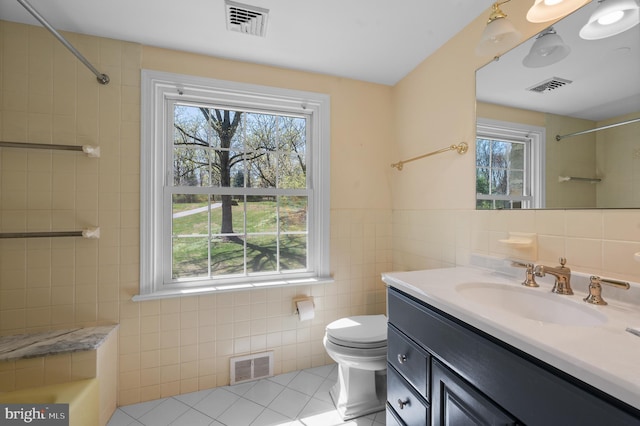 bathroom with tile walls, visible vents, and plenty of natural light