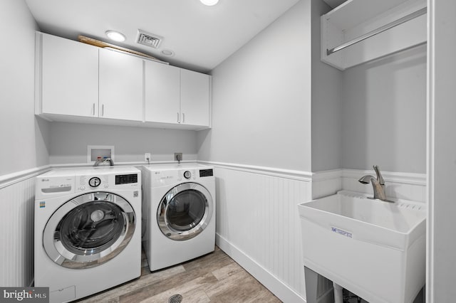washroom with a sink, wainscoting, visible vents, independent washer and dryer, and cabinet space