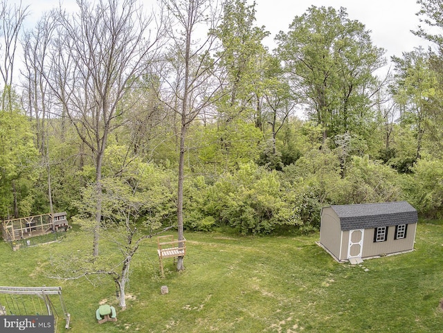 view of yard featuring an outdoor structure, a forest view, and a storage shed