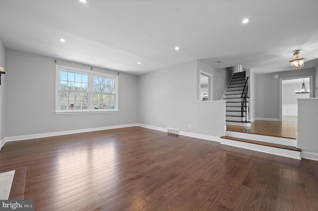 unfurnished living room featuring a chandelier, wood finished floors, visible vents, and stairs
