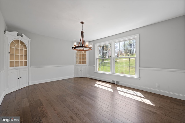 unfurnished dining area featuring dark wood finished floors, visible vents, baseboards, and a notable chandelier