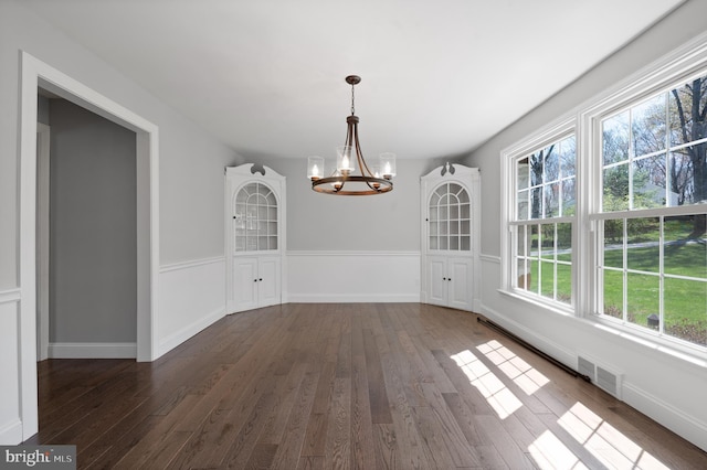 unfurnished dining area with dark wood-style floors, visible vents, a notable chandelier, and a healthy amount of sunlight
