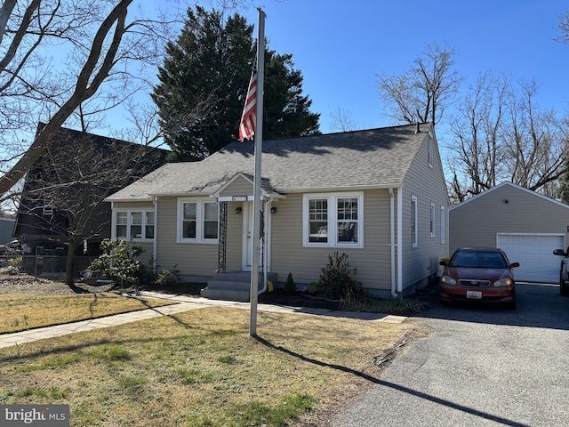 view of front of home featuring an outbuilding, roof with shingles, a detached garage, driveway, and a front yard