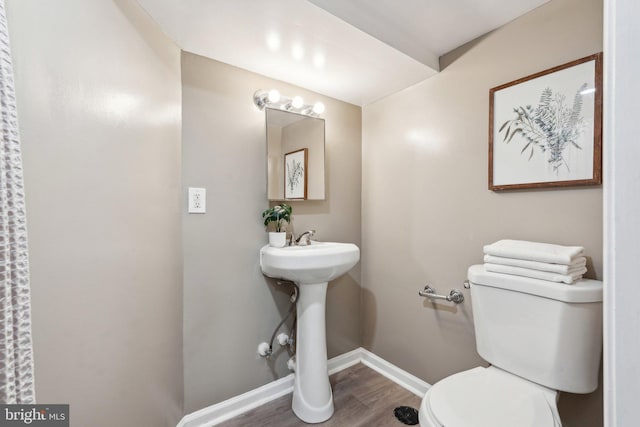half bathroom with toilet, baseboards, and wood finished floors