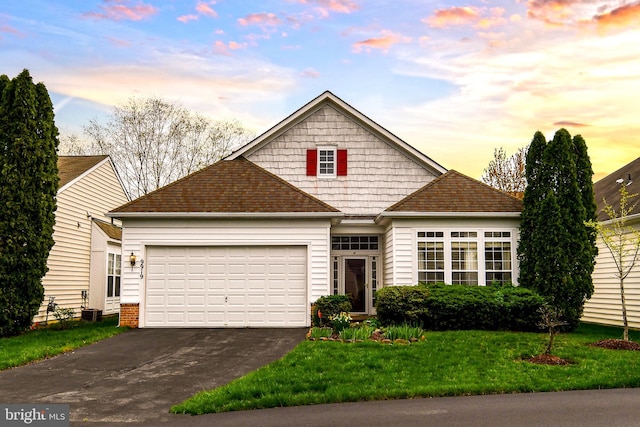 view of front facade with a yard, a shingled roof, a garage, and aphalt driveway