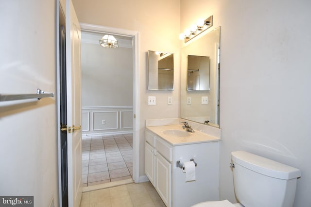 bathroom with a decorative wall, toilet, vanity, wainscoting, and tile patterned flooring