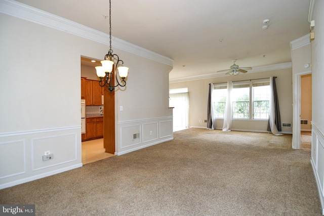 empty room featuring a decorative wall, crown molding, wainscoting, ceiling fan with notable chandelier, and light carpet