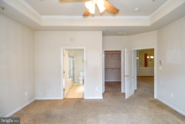 unfurnished bedroom with a raised ceiling, ornamental molding, and a walk in closet