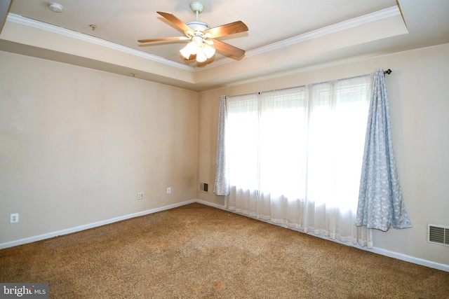 carpeted empty room with baseboards, a raised ceiling, crown molding, visible vents, and ceiling fan