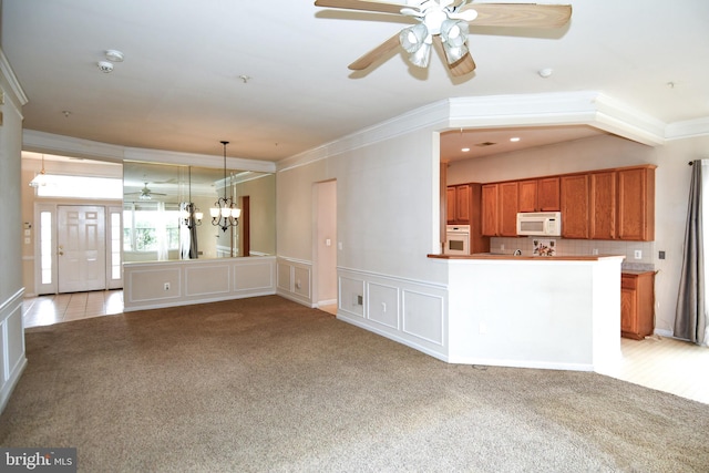 unfurnished living room with a decorative wall, crown molding, ceiling fan with notable chandelier, a wainscoted wall, and light colored carpet