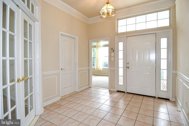 entrance foyer featuring light tile patterned floors, a decorative wall, a chandelier, crown molding, and wainscoting