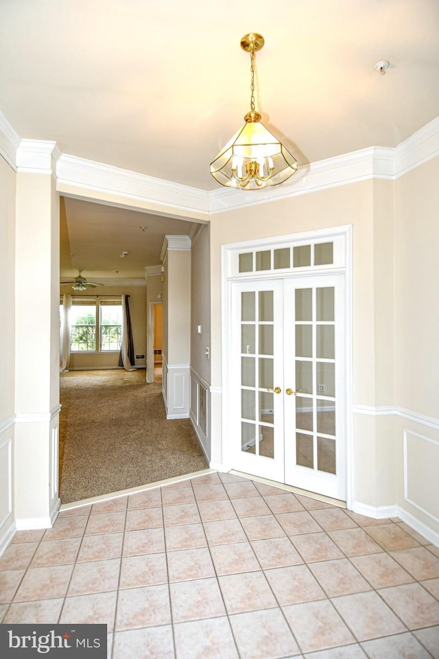 unfurnished room featuring french doors, crown molding, a decorative wall, and light tile patterned floors