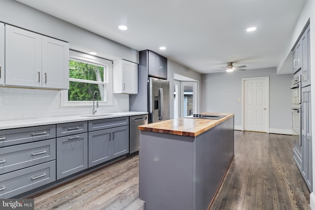 kitchen with a sink, stainless steel appliances, wood counters, dark wood finished floors, and gray cabinetry