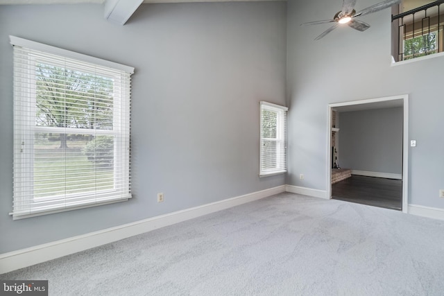 carpeted empty room featuring a towering ceiling, beamed ceiling, baseboards, and a ceiling fan