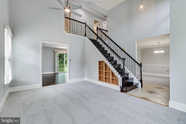unfurnished living room featuring baseboards, stairway, a high ceiling, and ceiling fan with notable chandelier