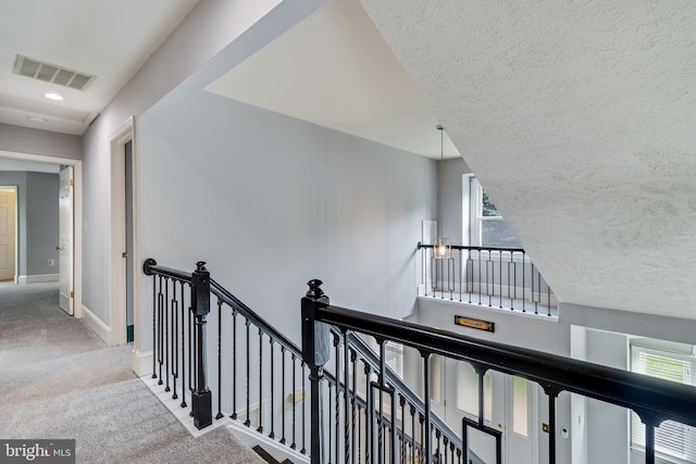 corridor featuring a textured ceiling, baseboards, carpet flooring, visible vents, and an upstairs landing